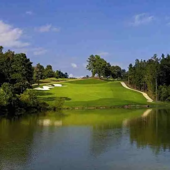 A green at Grand Oaks seen across a lake, with bunkers and pines on the far bank.