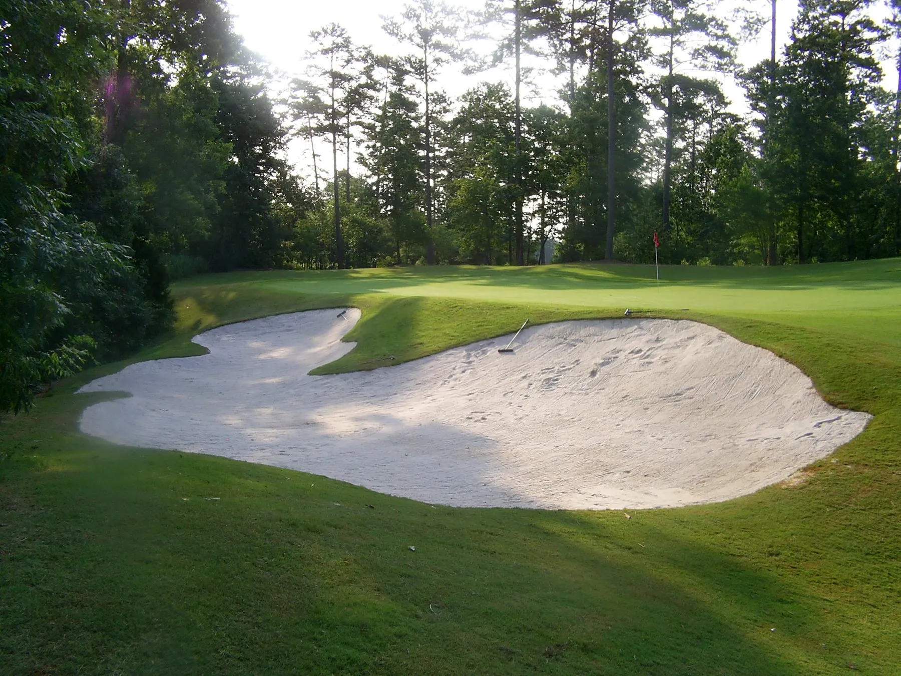 Two sand bunkers wrapping the front of a putting surface, with a red flag on the green beyond.