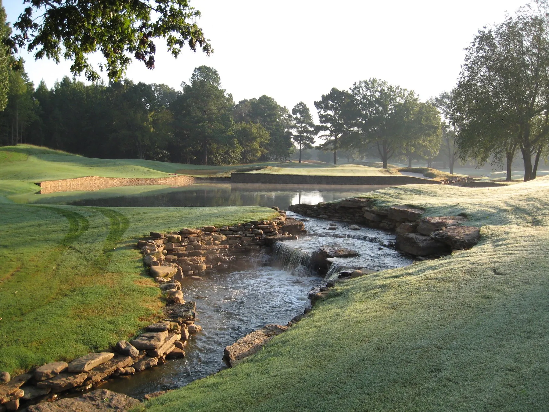 A rocky creek running down to a lake at Mirimichi, with a bunkered green across the water.