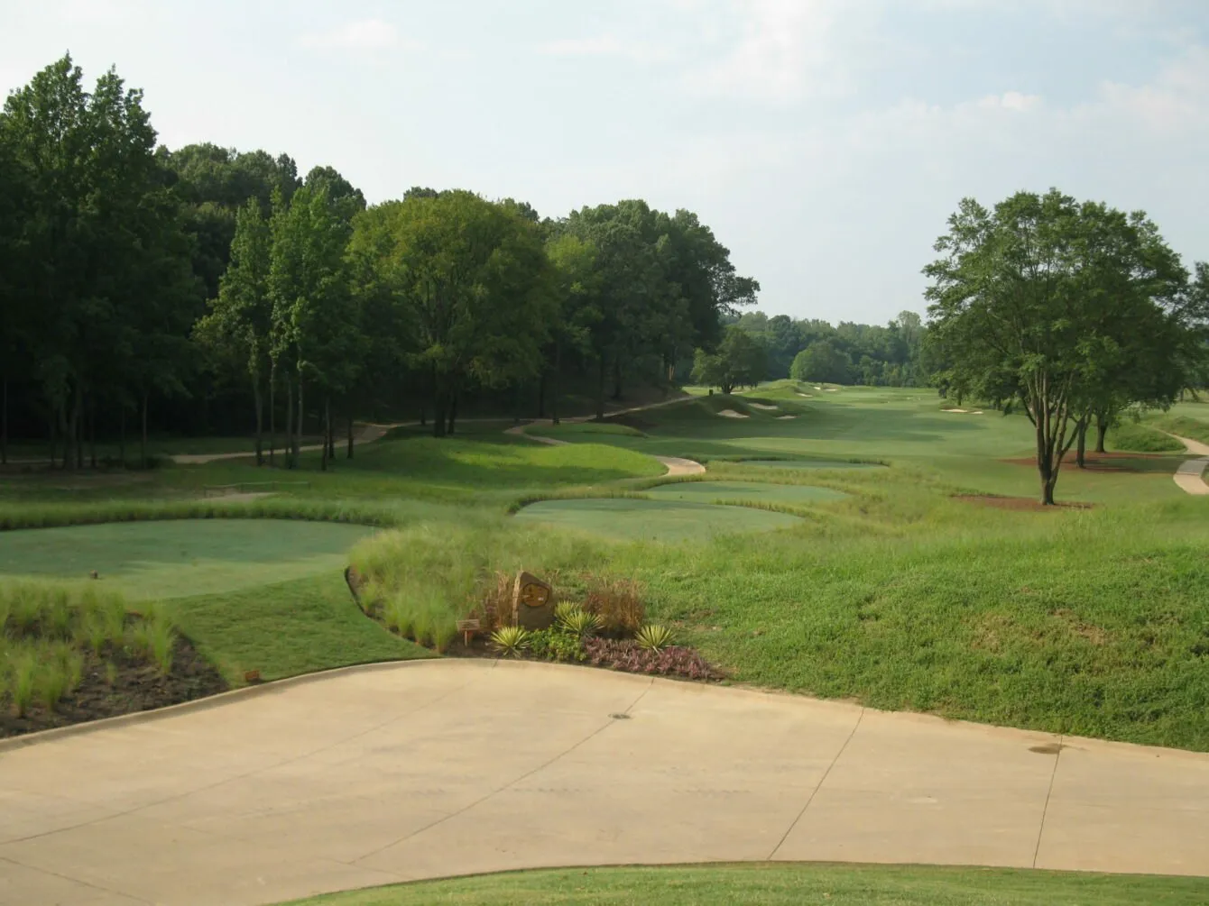 A cart path curving past a fairway lined with mature trees and a planted retaining bank.