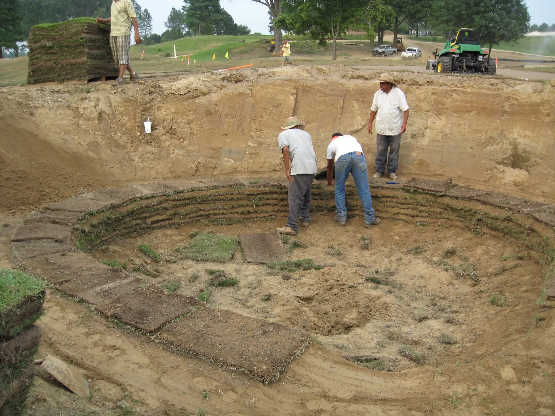 Two crew members work in the base of a bunker under construction at Mirimichi, with cut sod stacked above them.