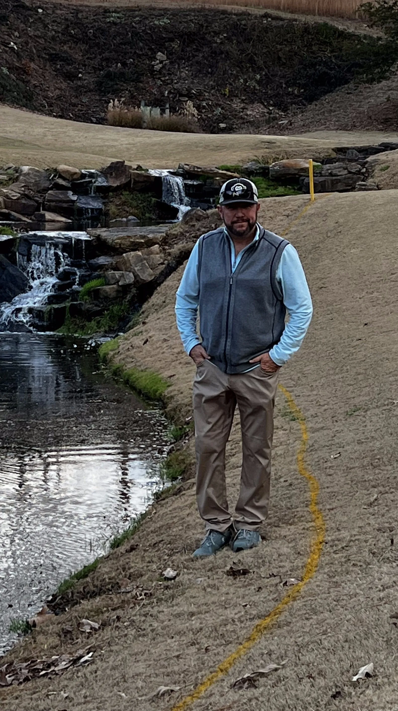 Randy Wilson standing beside a rock waterfall spilling into a pond on one of the company's golf courses.