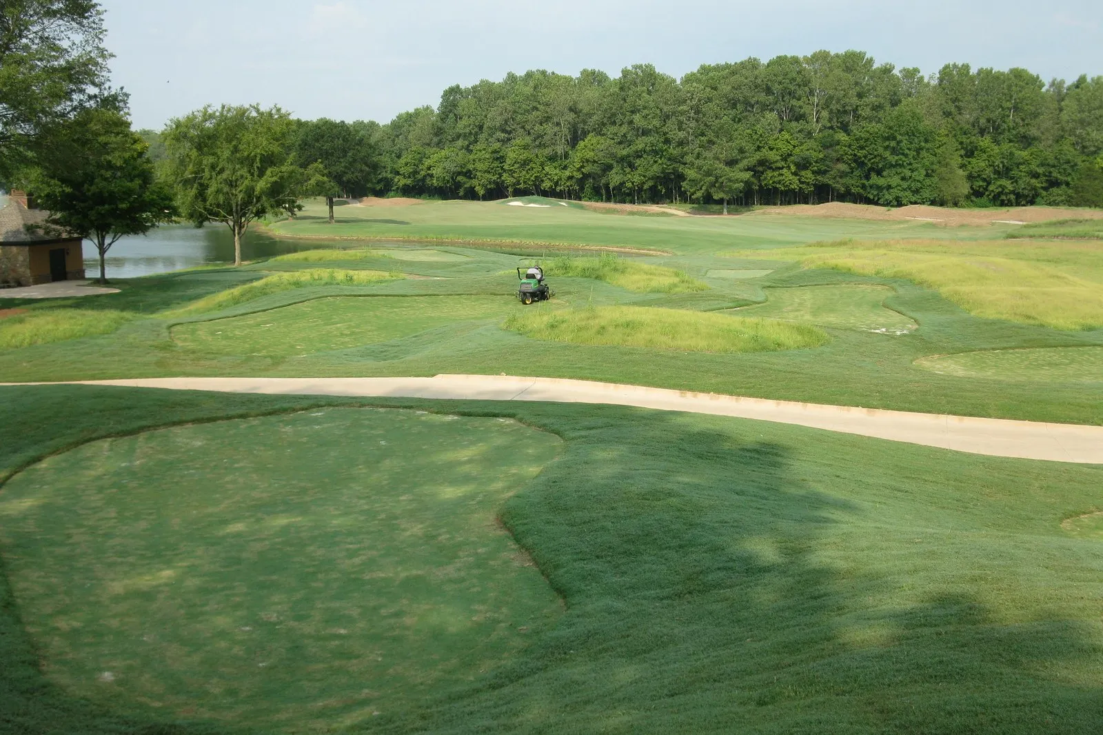 A wide view across a finished course — mown fairways, sand bunkers and a maintenance cart, with a lake and tree line beyond.