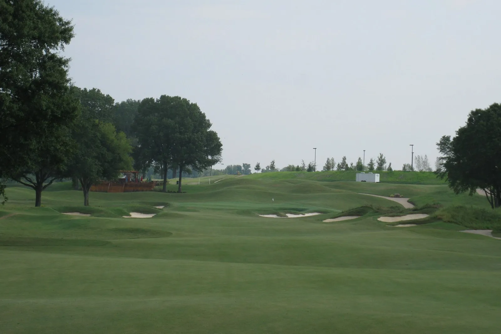 A broad mown fairway running between two tree lines toward a cluster of sand bunkers.